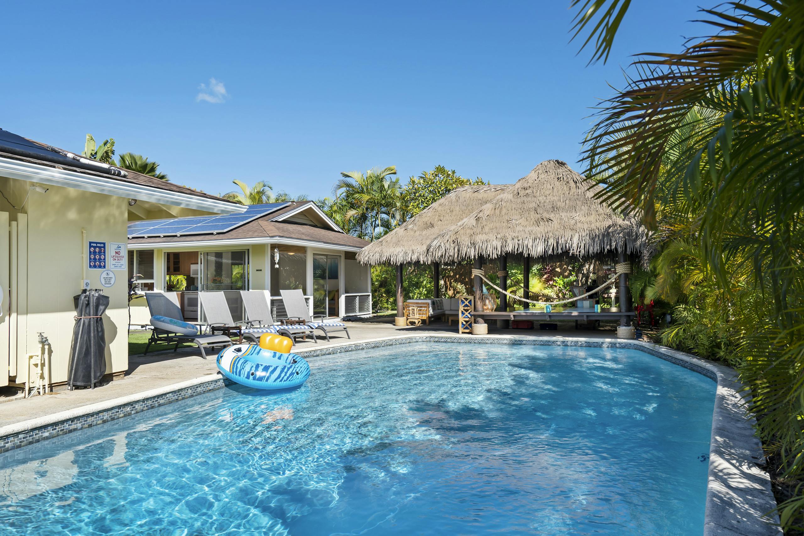 A serene tropical getaway featuring a swimming pool surrounded by lush greenery and thatched shade.